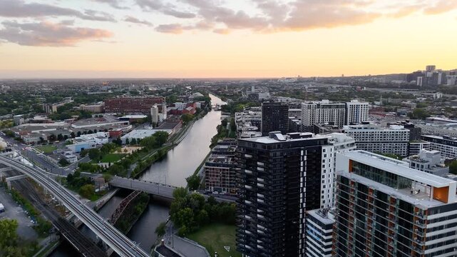 Passenger train passing through Griffintown, Montreal, Quebec, Canada at sunset with modern skyline. g