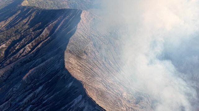 Dark, rugged slopes frame billowing volcanic smoke. Steam rises from earth ancient, molten core at Mount Bromo