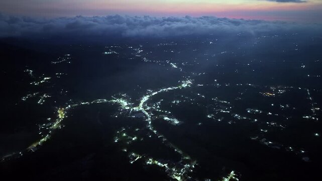 Misty twilight over mountain valley with scattered village lights beneath rolling clouds at Pronojiwo, East Java, Indonesia
