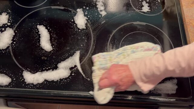 Wiping soapy cleaner off an electric glass stovetop with a cloth