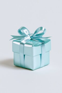 Minimal turquoise gift box with shiny satin ribbon and bow isolated on a light neutral background, vertical festive composition with generous copy space