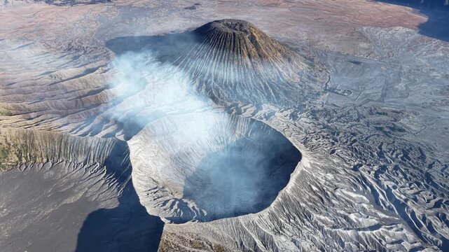 Volcano exhales mist from its crater. Rugged terrain surrounds the smoking peak at Bromo