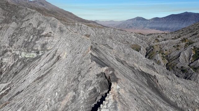 Aerial daytime drone panorama of Mount Bromo volcanic ridge with weathered ash slopes and distant mountain valley.