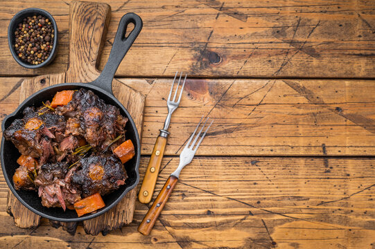 Braised beef oxtail stew with carrots and rosemary in cast iron skillet on rustic wooden table, rich dark sauce
