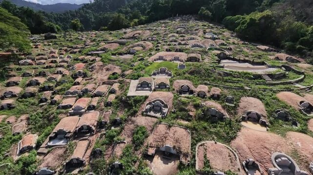 Aerial view of Chinese stone tombs on a hillside. Green grass grows between rounded burial chambers at Mount Erskine, Penang