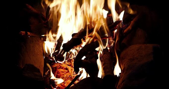 Bright campfire burning with glowing flames and wood logs surrounded by stones at night.