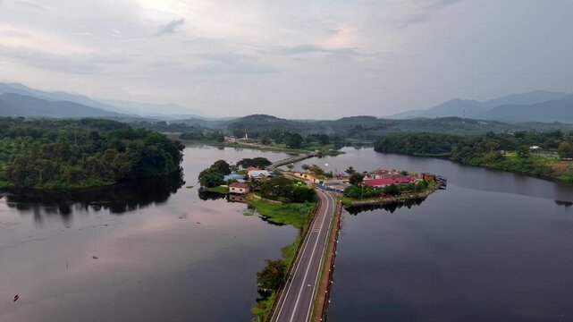 Aerial drone view captures a bridge crossing a wide lake. Forested islands dot the calm water at Tasik Raban