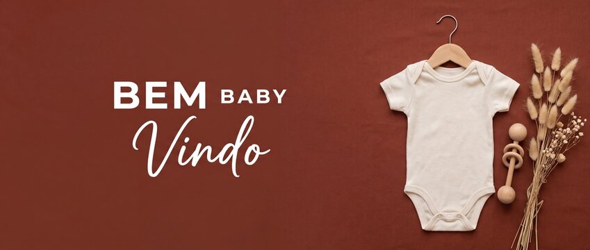 Baby onesie flat lay mockup with Bem Vindo Portuguese welcome text on brown background, featuring minimalist neutral organic newborn bodysuit, wooden hanger, rattle, and dried lagurus plants.