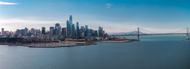 Fototapeta na wymiar Aerial wide view of San Francisco downtown skyscrapers, Salesforce Tower, marina harbour, and the Oakland Bay Bridge spanning over the calm bay water on a clear day.
