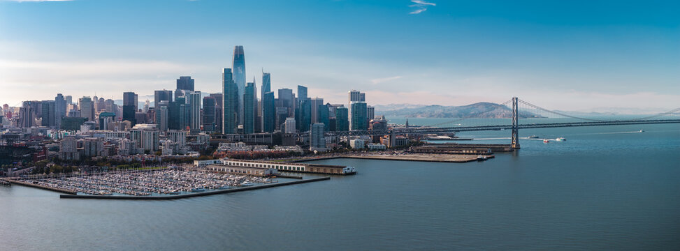 Aerial shot of the San Francisco downtown skyline, Embarcadero waterfront marina, Salesforce Tower, and Oakland Bay Bridge stretching across the bay waters on a clear sunny day.
