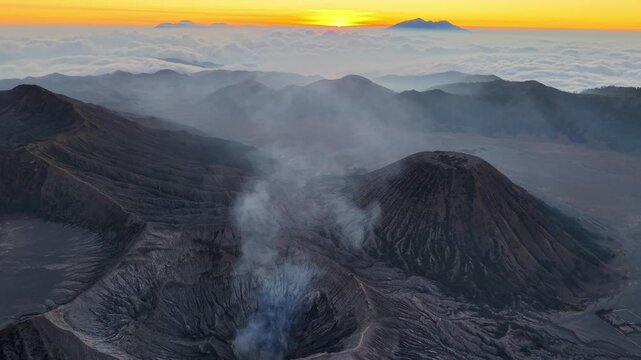 Golden sun peeks over volcanic Mount Bromo peaks. Smoke drifts from active crater mouth