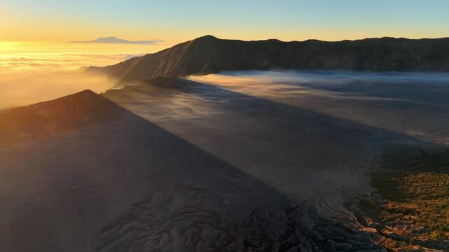 Mist drifts over mountain ridges at dawn. Sunlight glints off volcanic slopes at Bromo
