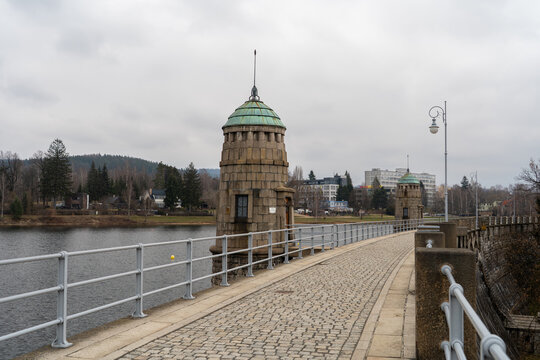 Historic dam tower and walkway at Mseno Reservoir in Jablonec nad Nisou, Liberec Region, Czech Republic, with the reservoir, hills and city buildings beyond.