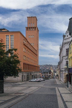 Historic street and urban architecture in Jablonec nad Nisou, Liberec Region, Czech Republic, with colorful buildings, a sloping road and wooded hills beyond.