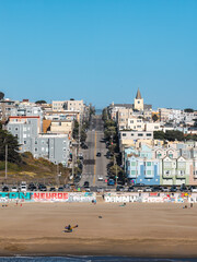 Fototapeta premium Ocean Beach seawall painted with graffiti fronts a sloping residential street with pastel houses and church steeple in San Francisco, California, viewed across wide sand.