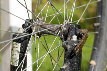 Dirty mountain bike front wheel assembly showing hub, metal spokes, axle, fork, rim, tire, fastener and bearing details, close view of used bicycle hardware for repair, maintenance and engineering © PhotoFed