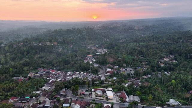 Drone sunrise panorama over misty tropical village and forested hills near Tumpak Sewu, East Java