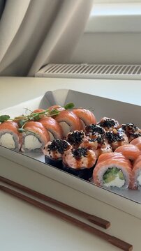 Sushi set of 3 rolls in paper packaging with wooden sticks laying down on the table at home. Sushi asian food delivery to home, japanese cuisine, philadelphia roll and felix roll with salmon