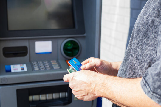 Close-up of a man holding a credit card and money while using an automated teller machine