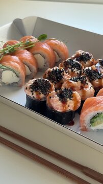 Sushi set of 3 rolls in paper packaging with wooden sticks laying down on the table at home. Sushi asian food delivery to home, japanese cuisine, philadelphia roll and felix roll with salmon close up