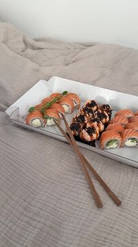 Sushi set of 3 rolls in paper packaging with wooden sticks laying down on the bed at home. Sushi asian food delivery to home, japanese cuisine, philadelphia roll and felix roll with salmon