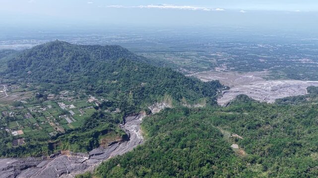 High altitude wide panorama of an expansive, empty volcanic sediment basin left dehydrated and barren below the mountain ridges of Lumajang.