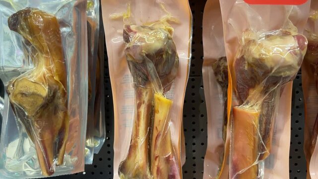 Close-up cured marrow bones in clear vacuum-sealed plastic pouches under retail lighting. Packaged animal bones sold as food for dogs.