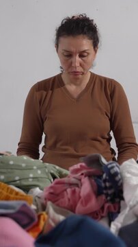 Textile waste, fast fashion. Woman sorting through her overflowing wardrobe at home, reviewing old and unused clothing