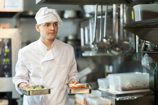 Busy young male cook carrying ingredients in containers in professional restaurant kitchen