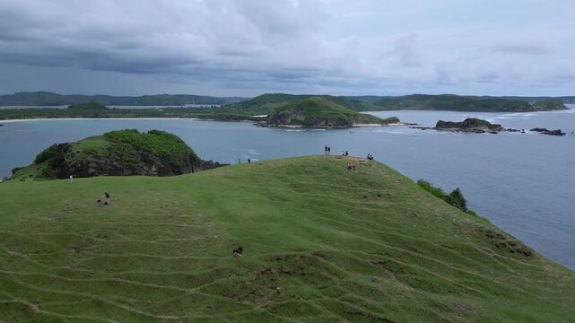 Friends Watching Storm Clouds Gather Over Bay From Grassy Headland, Brooding Sky And Dark Water Create Dramatic Atmosphere, Aerial View Shows Island Silhouettes, Shoreline Paths, Lombok