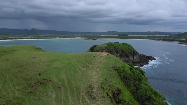 Wide Drone Shot Rugged Coastline And Ocean Under Moody Sky Deep Blue Water, Crashing Waves On Basalt Cliffs, Distant Islets, Group of Tourists, Bukit Merese, Lombok, Tanjung Ann