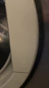 Close-up of a washing machine or tumble dryer drum placed in an urban environment. Metallic circular laundry appliance detail contrasts with the surrounding city setting ay night.