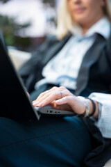 Fototapeta premium Close-up shows a woman's hand using a laptop touchpad and typing during outdoor work, with a black business suit and a remote workspace setting.