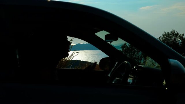 Heat inside the car. Silhouette of a woman using a portable fan to cool down while suffering from heatstroke in the car during a hot summer