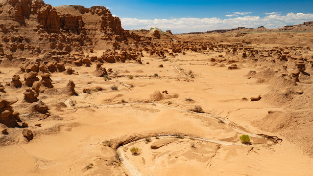 A low aerial view (facing south) inside the Valley of the Goblins of Goblin Valley State Park, Utah. A dried up creek bed meanders downhill through the sand and clay.