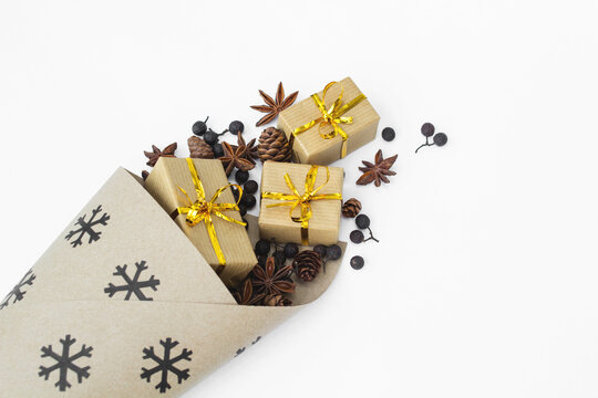Close-up overhead view of wrapped Christmas gifts, pinecones, star anise and berries spilling out of a snowflake patterned paper cone