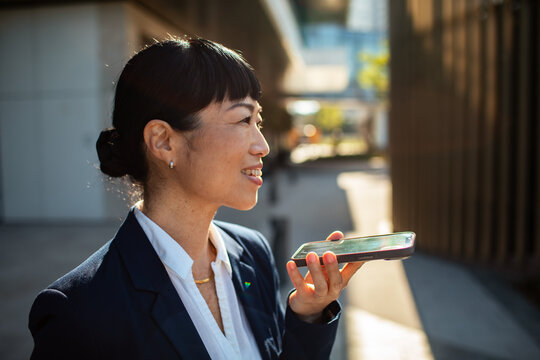 Smiling businesswoman using voice assistant on smartphone outdoors