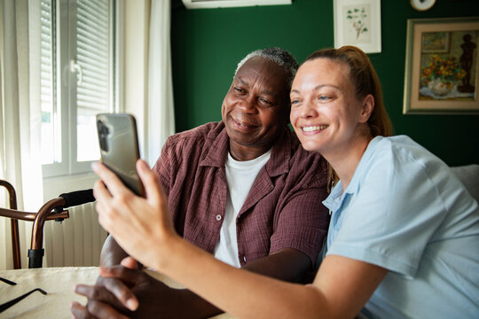 Caregiver and senior man taking a selfie at home