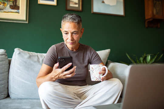 Senior woman using smartphone with coffee on sofa
