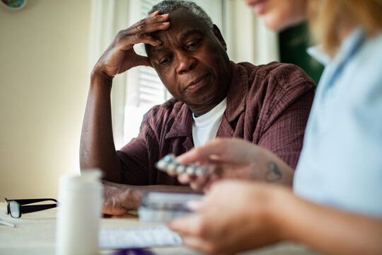 Caregiver reviewing pills with senior man at home