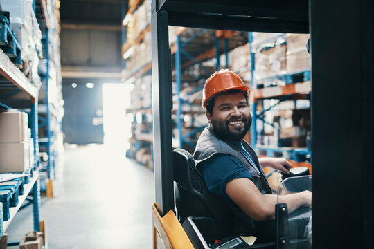 Smiling warehouse worker driving a forklift in a warehouse aisle