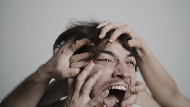 Close up of man screaming in agony with hands gripping face showing intense distress and pain