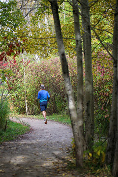 un homme fait son jogging dans un parc bois&eacute; en automne.