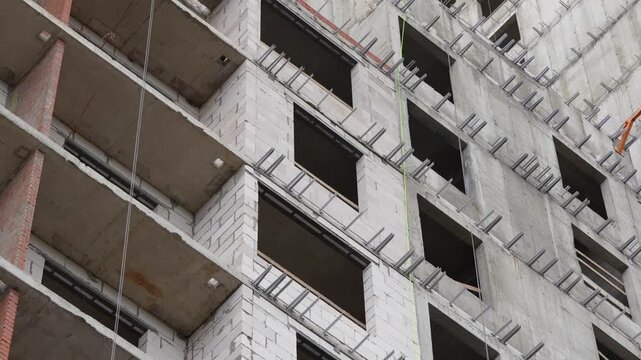 Partially completed high rise facade with installed windows, exposed concrete, masonry walls and metal brackets prepared for exterior cladding installation