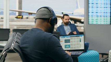Fototapeta premium Casual startup representative checks insights and evaluation data on a laptop in an airport lounge, preparing a briefing for an international meeting abroad during a modern global business trip.