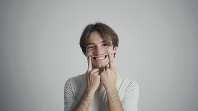 Young man in white shirt posing with funny face and hands stretching cheeks