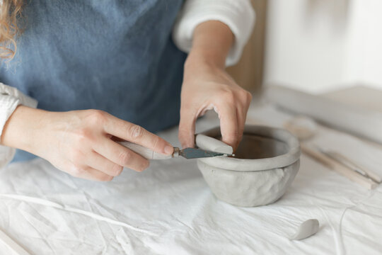 Woman potter meticulously shaping clay in a studio setting, demonstrating a creative and focused approach, captured in a close-up side view, the scene showcases.