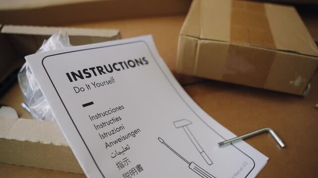 Close up on a do it yourself instruction manual on a cardboard box containing furniture parts and tools, ready for assembly. Easy to use, user friendly, self assembly and home improvement