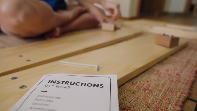 Detailed view of do it yourself instruction manual for assembling flat pack furniture, with a person working on the wooden parts in the background, carefully following the guide screwing with wrench