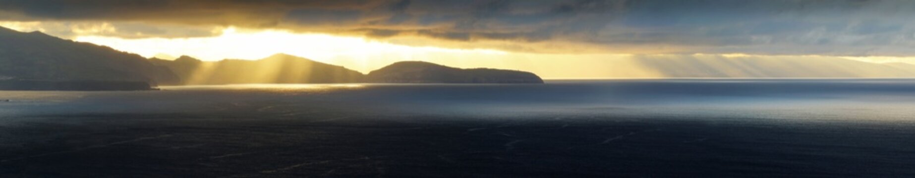 Sun rays breaking through cloud over the sea at sunset, with an island on the horizon, Azores, Portugal, October 2017